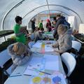 Children drawing at table in large greenhouse polytunnel at City Farm, Oxford