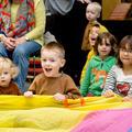 Children sat on the floor, singing and holding on to a brightly coloured play parachute