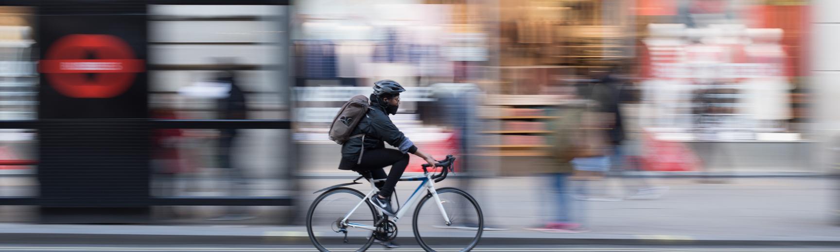 Blurred image of a cyclist cycling down a London street, past a bus stop and shops