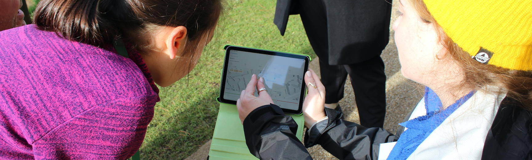 A child watches as a researcher explains data on an ipad screen outside on a sunny day