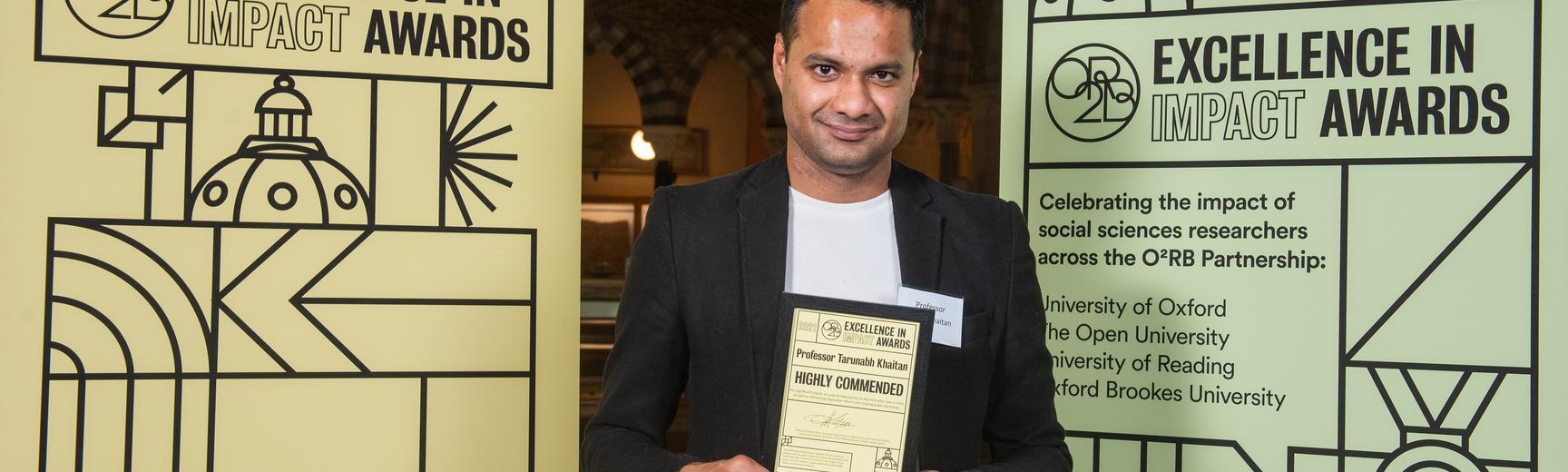 Professor Tarunabh Khaitan holds his Highly Commended impact award, flanked by event branding at the awards reception