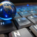 A small glass marble representing the Earth sits on a computer keyboard