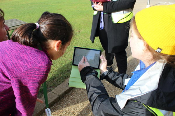 A child watches as a researcher explains data on an ipad screen outside on a sunny day