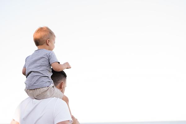 A young boy sits on his father's shoulders. The father holds the boy's ankles to stabilise him.