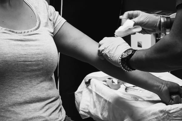 A black and white image of a medical professional, who is wearing gloves, preparing a patient's arm for an injection