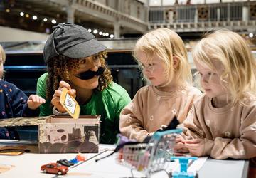 Researchers engage curious minds at the 2024 Festival of Social Science A researcher dressed up as a detective shows two young children an email symbol