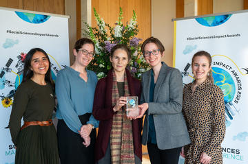The OPHI team smile and hold their prize trophy. In the background is the Impact Awards branding and a flower arrangement.