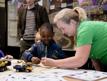 A you g boy interacts with a toy digger and an event volunteer