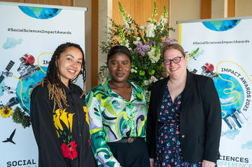 Dr Zaahida Nabagereka, Dr Lesley Nelson-Addy and Dr Velda Elliott smile to camera.  In the background is the Impact Awards branding and a flower arrangement.