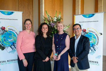 Four Young Lives team members smile and hold the Developing Impact trophy. In the background is the Impact Awards branding and a flower arrangement.